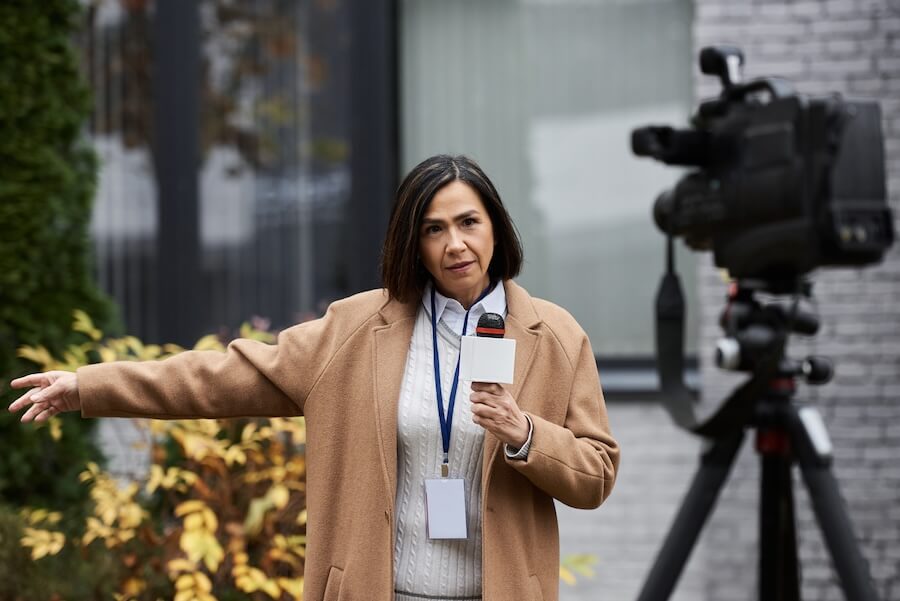 A multiracial female journalist in a beige coat stands confidently, holding a microphone and broadcasting live. Headshot of Alex Lefkowitz the ceo and founder of Tasty Edits