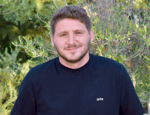 ScorePlay customer headshot. Man smiling in front of green foliage. ScorePlay customer story.